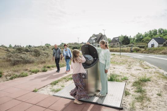 2 kinderen droppen afval correct in de afvalcontainer - de grootouders kijken er blij naar