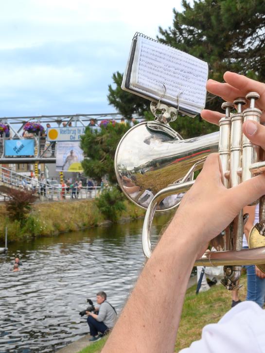 Trompetspeler speelt en kijkt in de richting van het kanaal en de voetgangersbrug in Adinkerke.